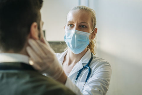 Doctor Wearing Surgical Mask Examining Man