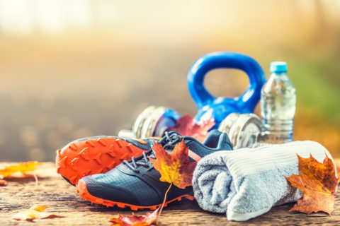 Pair Of Blue Sport Shoes Water And Dumbbells Laid On A Wooden Board In A Tree Autumn Alley With Maple Leaves Accessories For Run Exercise Or Workout Activity.